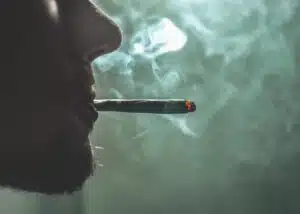 The image shows a man smoking what appears to be a drug, most likely cannabis. It is a close up shot and his identity is not known.