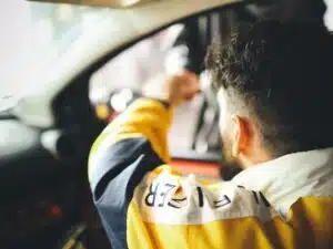 A man being pulled over in his car. The image shows the man sitting inside the car and reaching out of his open window and handing something to somebody on the other side.