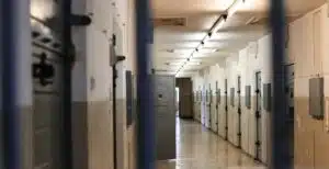 An image taken through the bars of a prison gate looking into a row of prison cells.